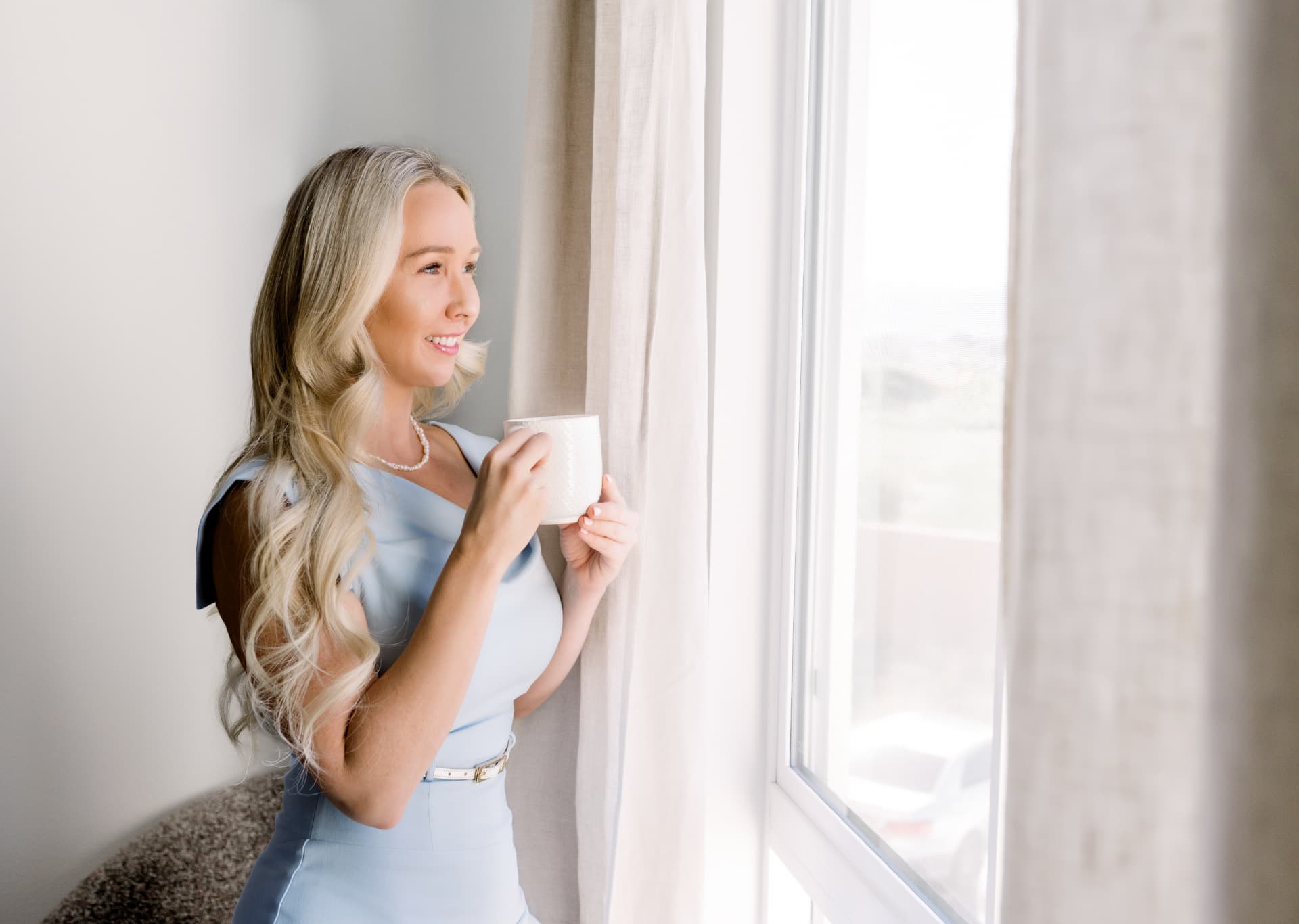 Amelia looking out a window with a cup of coffee