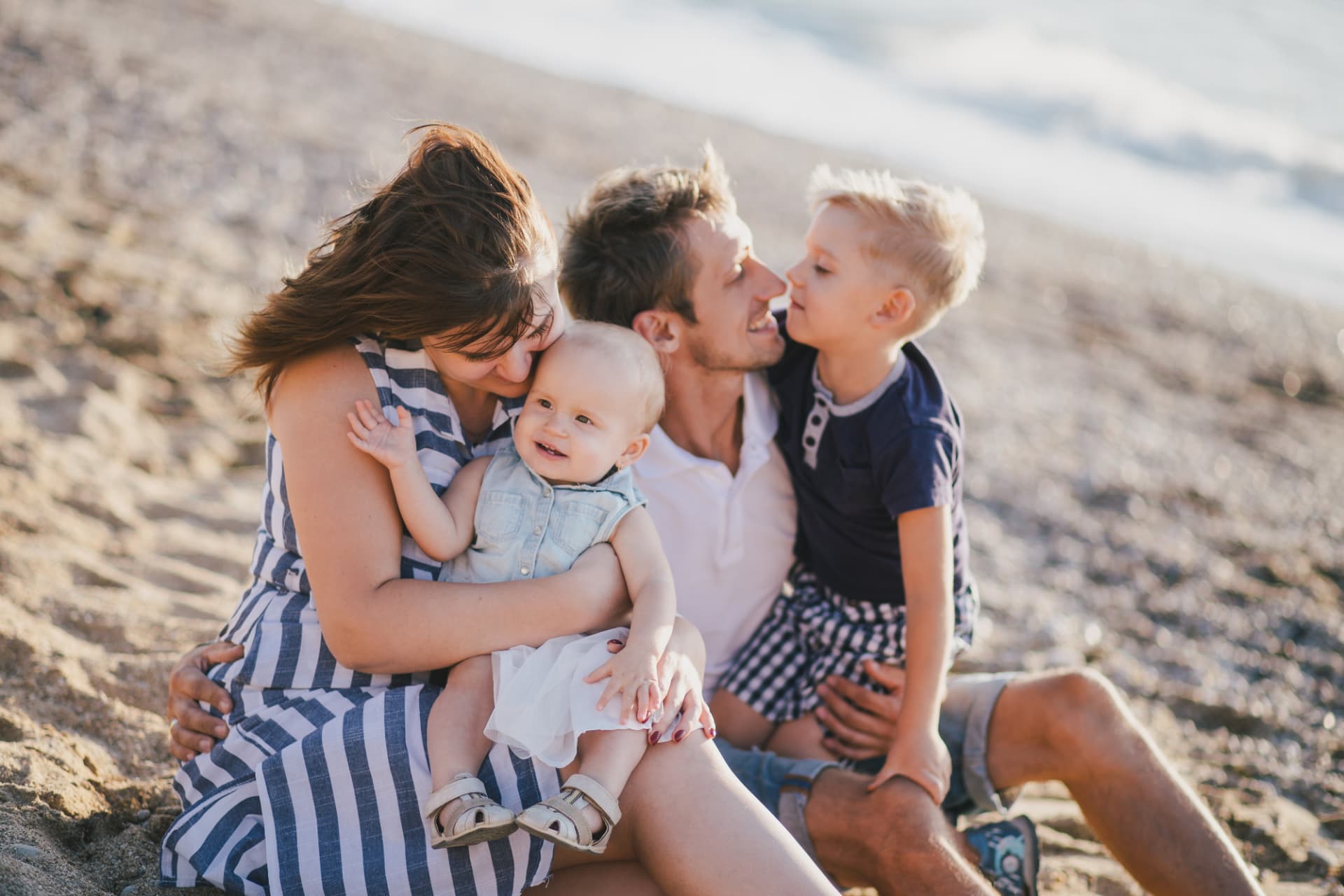 Mother, father and two young children sitting together on a sandy shore in warm afternoon light