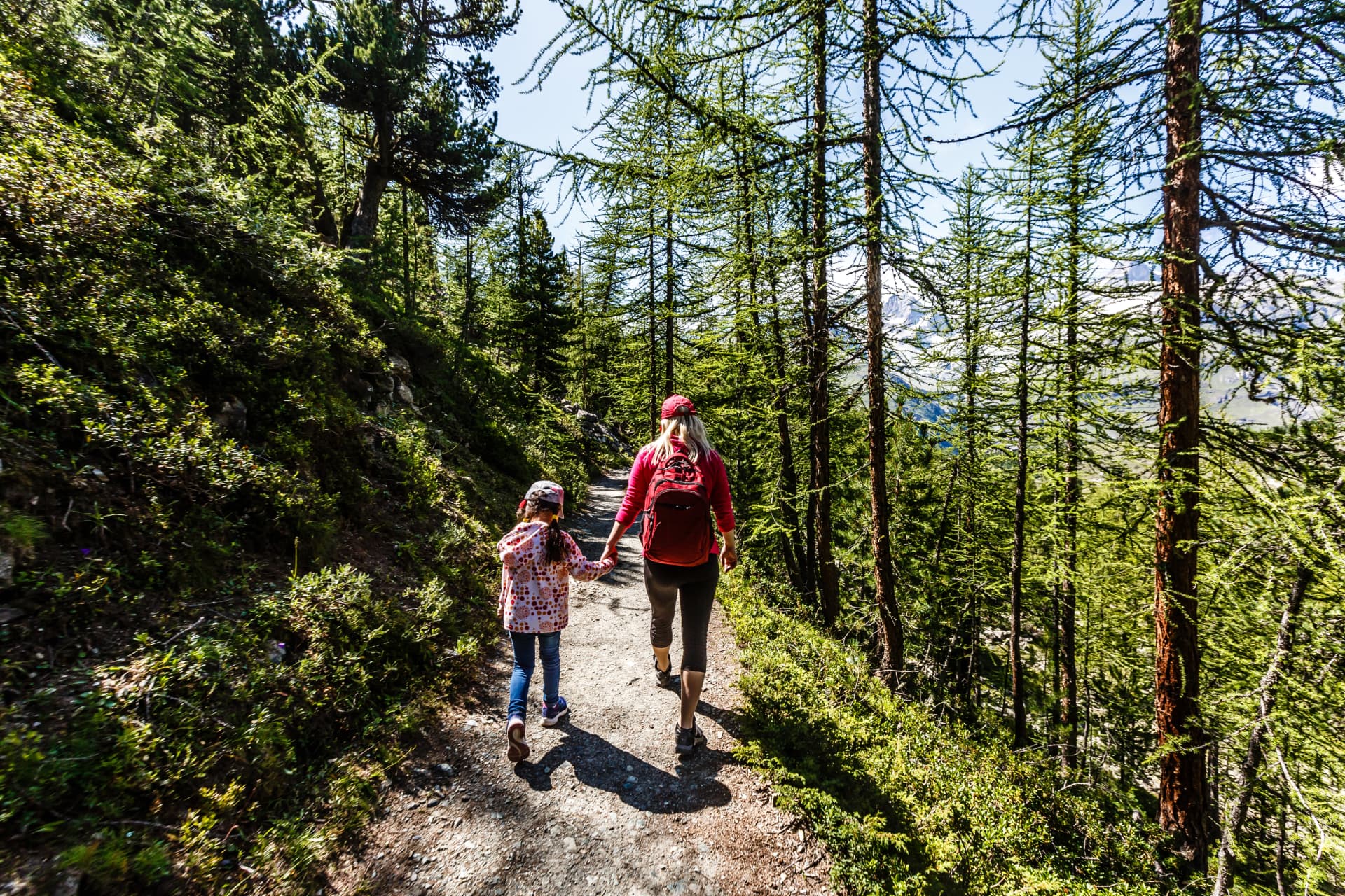 Family of two walking together on a mountain trail in cool morning light, seen from behind